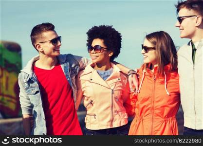 friendship, tourism, travel and people concept - group of happy teenage friends in sunglasses hugging and talking on city street
