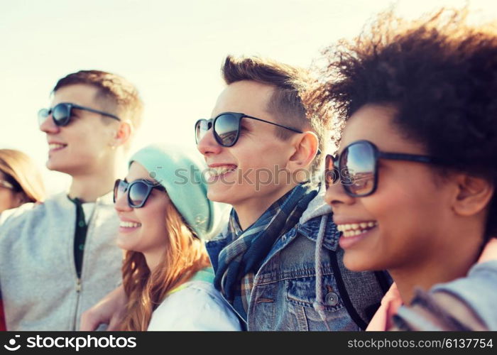 friendship, tourism, travel and people concept - group of happy teenage friends in sunglasses hugging outdoors