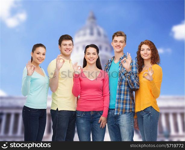 friendship, tourism, travel and people concept - group of smiling teenagers showing ok sign over white house background