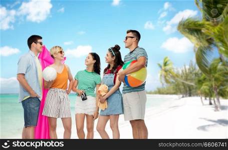 friendship, travel and summer holidays concept - group of happy smiling friends in sunglasses with ball, volleyball, towel, camera and air mattress over tropical beach background in french polynesia. friends with beach supplies over exotic landscape