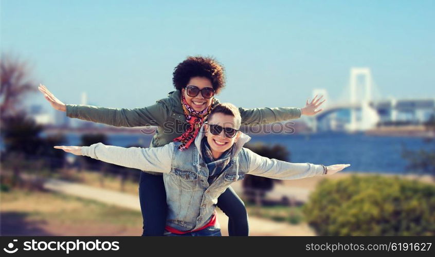 friendship, travel, tourism and people concept - happy international teenage couple in shades having fun over rainbow bridge at tokyo in japan background