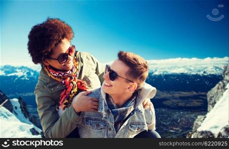 friendship, travel, tourism and people concept - happy international teenage couple in shades having fun over alps mountains in austria background