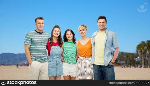 friendship, travel, tourism and summer holidays concept - group of happy smiling friends hugging over venice beach background in california. happy friends hugging over venice beach