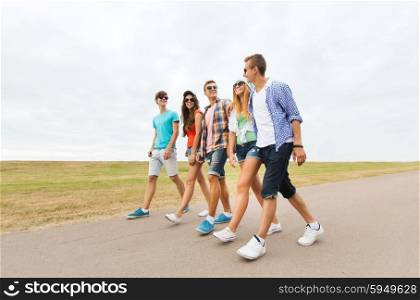 friendship, travel, tourism, summer vacation and people concept - group of smiling teenagers walking on road