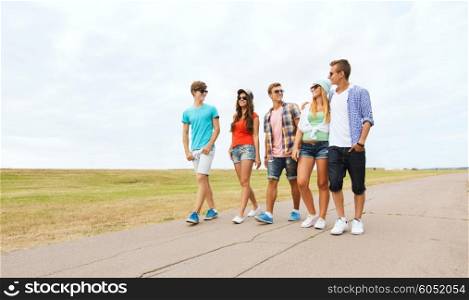 friendship, travel, tourism, summer vacation and people concept - group of smiling teenagers walking on road