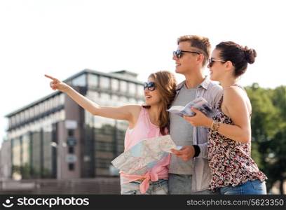 friendship, travel, tourism, vacation and people concept - smiling friends with map and city guide pointing finger outdoors