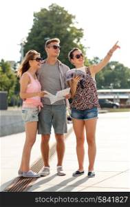 friendship, travel, tourism, vacation, summer and people concept - smiling friends with map and city guide pointing finger outdoors