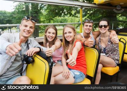 friendship, travel, vacation, summer and people concept - group of happy friends with digital camera traveling by tour bus and showing thumbs up
