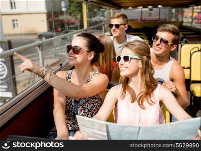 friendship, travel, vacation, summer and people concept - group of smiling friends with map traveling by tour bus