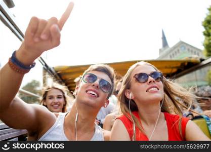 friendship, travel, vacation, summer and people concept - smiling couple with earphones traveling by tour bus and pointing finger