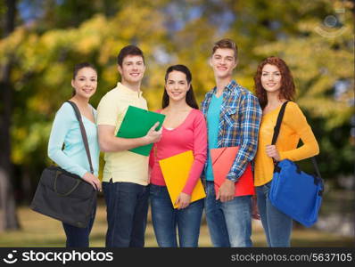 friendship, vacation, education and people concept - group of smiling teenagers with folders and school bags over park background