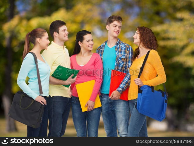 friendship, vacation, education and people concept - group of smiling teenagers with folders and school bags over park background