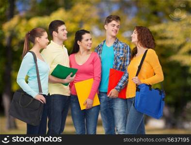 friendship, vacation, education and people concept - group of smiling teenagers with folders and school bags over park background