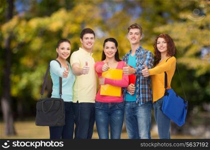 friendship, vacation, education, gesture and people concept - group of smiling teenagers with folders and school bags showing thumbs up over park background