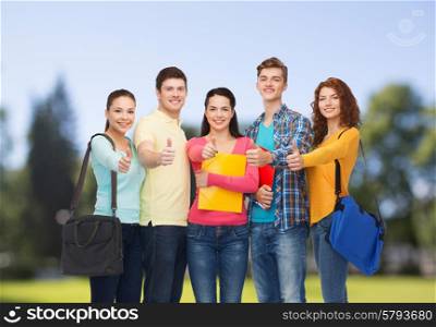 friendship, vacation, education, gesture and people concept - group of smiling teenagers with folders and school bags showing thumbs up over park background