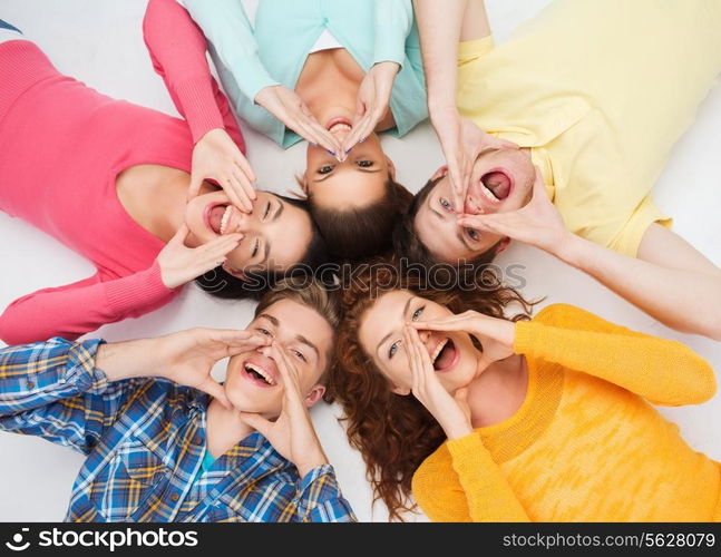 friendship, youth, gesture and people - group of smiling teenagers lying on floor in circle and shouting