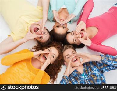 friendship, youth, gesture and people - group of smiling teenagers lying on floor in circle and shouting