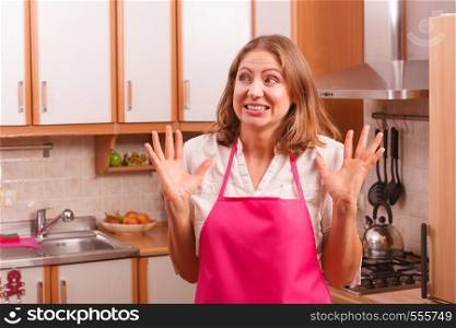 Frightened and worried woman wearing pink apron. Unhappy anxious and stressed housewife in kitchen. Negative facial emotion.. Unhappy housewife in kitchen