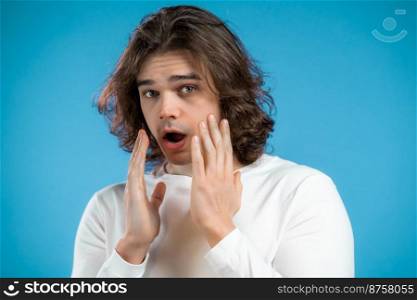 Frightened man shocked isolated on blue background. Stressed and depressed guy with long hairstyle because of bad news. High quality photo. Frightened man shocked isolated on blue background. Stressed and depressed guy with long hairstyle because of bad news