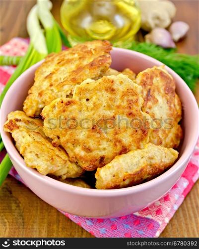 Fritters minced chicken in a pink bowl, napkin, oil, dill, garlic, ginger, green onions on a wooden board