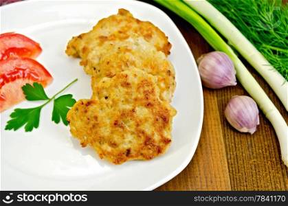 Fritters with chicken meat on a white plate with tomato and parsley, dill, onion, garlic on a wooden board