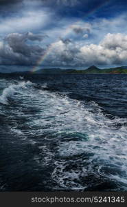 from a boat the rainbow from ocean and island in background