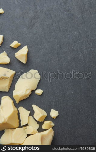 From above gray surface with composed pieces of organic pure raw cocoa butter in corner. Cocoa butter chunks as background