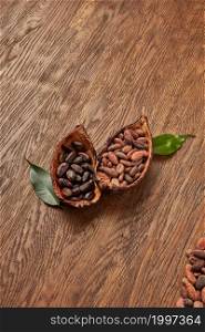 From above of composed halves of organic pods filled with piles of unpeeled and peeled cocoa beans placed on wooden surface with green leaves. Halved cocoa pods with peeled and unpeeled beans