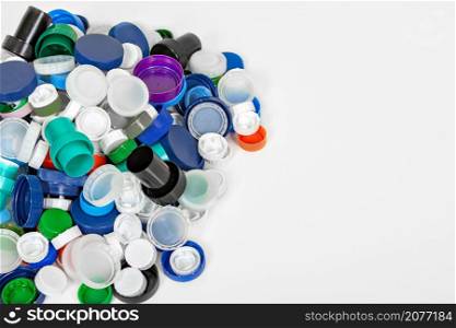From above of different colorful plastic lids stacked on white background for concept of recycling. Heap of plastic caps on table