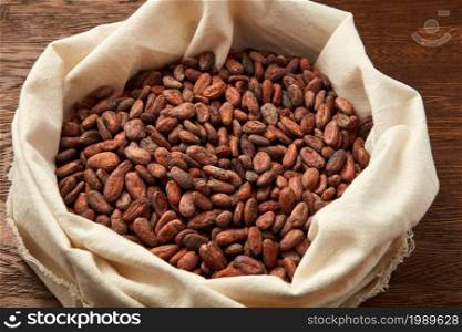 From above of fabric sack filled with raw fresh unpeeled beans of Theobroma tree on wooden surface. Unpeeled organic cocoa seeds in bag