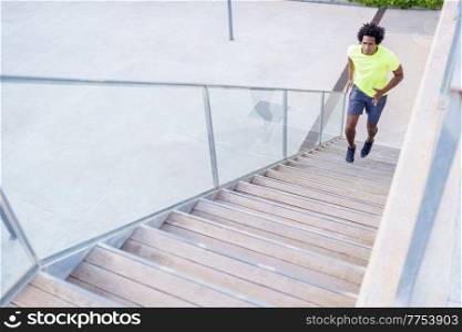 From above of fit African American male runner jogging up staircase during cardio training in city in summer. Black sportsman running upstairs in the city