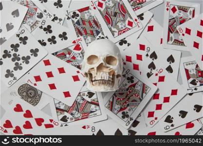 From above of human skull model placed on top of scattered deck of playing cards as concept of life and death gambling. Skull on scattered playing cards