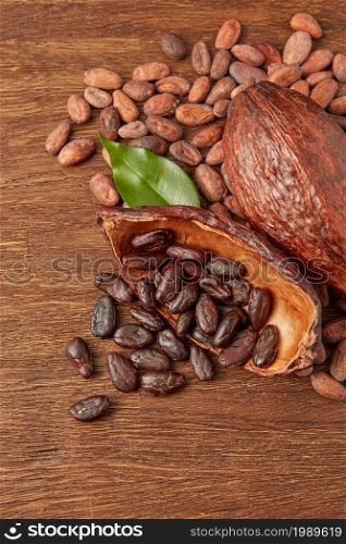 From above of whole and halved cocoa pods with pile of dark raw peeled and unpeeled cocoa beans on wooden surface. Scattered raw cocoa beans and pods