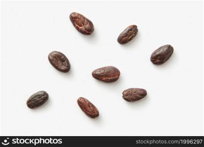 From above scattered small pile of organic beans of Theobroma cacao tree on light white background. Few aromatic fresh cocoa beans