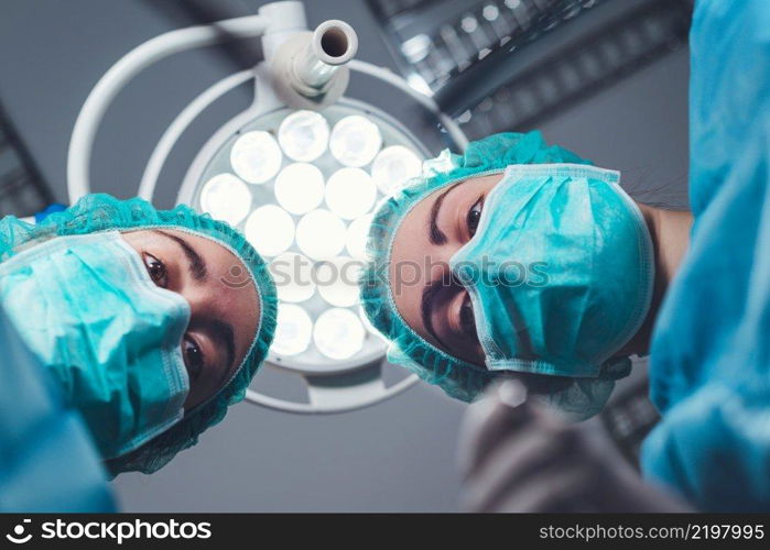 From below female surgeons in medical uniform using professional tools while standing under bright light in operating theater. High quality photo. From below female surgeons in medical uniform using professional tools while standing under bright light in operating theater