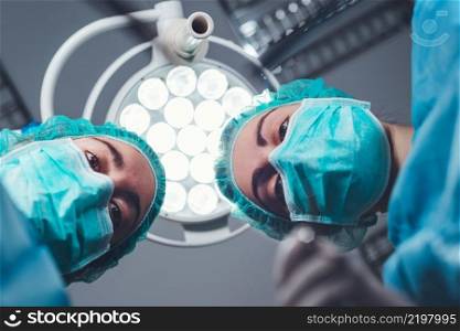 From below female surgeons in medical uniform using professional tools while standing under bright light in operating theater. High quality photo. From below female surgeons in medical uniform using professional tools while standing under bright light in operating theater