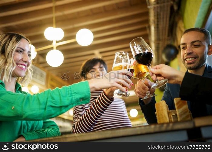 From below happy diverse male and female friend clinking glasses of alcohol during party in weekend in pub. Man and women proposing toast during party