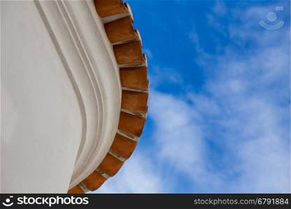 from bottom view on edge round roof of old house with red tiles on background of sky