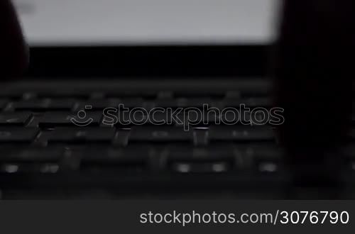 Front Close up of a male hand typing in dark room with laptop backlit keyboard.