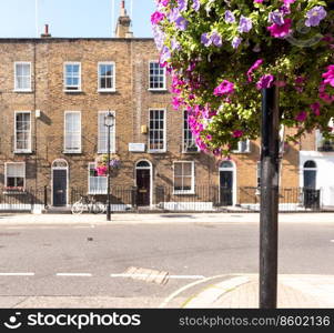 Front facades and arched doors of historic brick London Terrace houses with tall windows and iron railing out front with a bicycle on the sidewalk and l&post