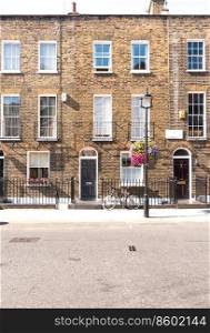 Front facades and arched doors of historic brick London Terrace houses with tall windows and iron railing out front with a bicycle on the sidewalk and l&post