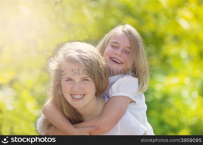 Front forward view, with focus on face of older girl, of sisters sharing a close moment while outdoors. Light haze effect applied to image.