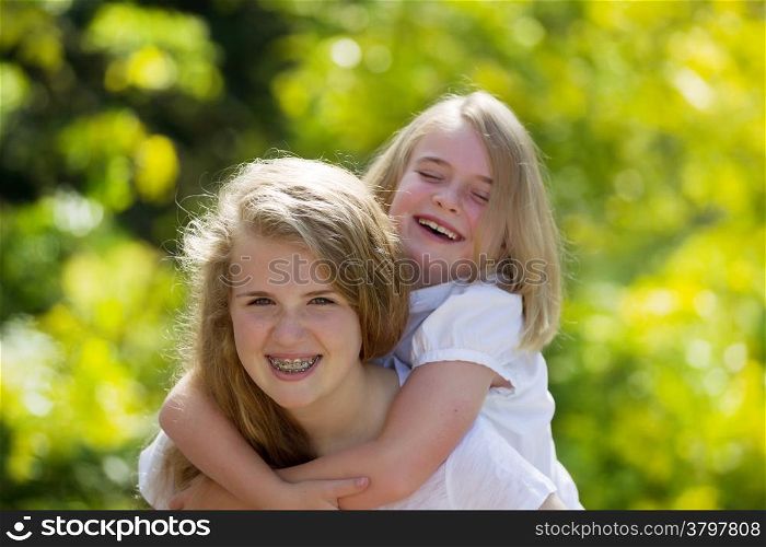 Front forward view, with focus on older sister, of oldest sister holding younger sister on her back while laughing together
