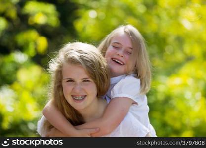 Front forward view, with focus on older sister, of oldest sister holding younger sister on her back while laughing together