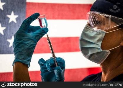 Front Line Worker Holding Syringe and Vial Filled with Coronavirus Vaccine or Medicine Silhouetted Against American Flag.