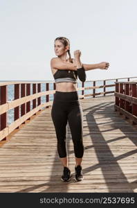 front view athletic woman stretching outdoors by beach