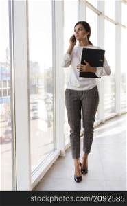 front view businesswoman holding binder talking phone