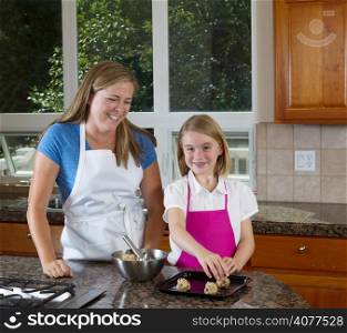 Front view, child looking forward, of mother and her younger daughter making cookies from raw dough