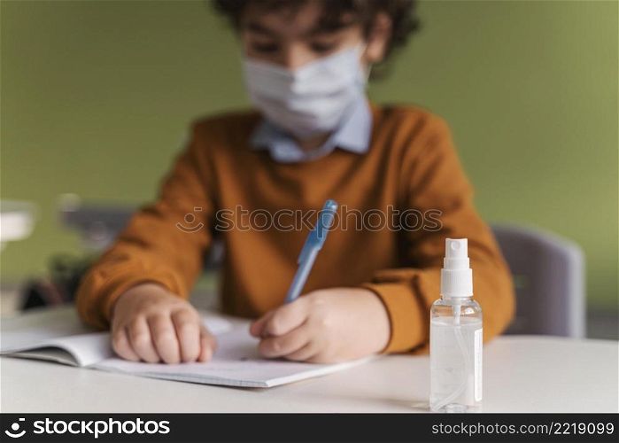front view child with medical mask class with bottle hand sanitizer desk