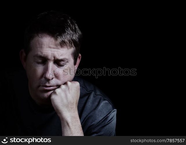 Front view close up of mature man with his eyes closed and chin in hand displaying depression on black background